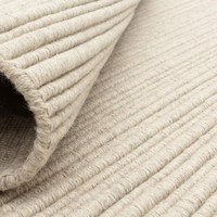 Close-up of a rolled cream wool rug demonstrating its flexibility, thickness, and natural yarn weave.