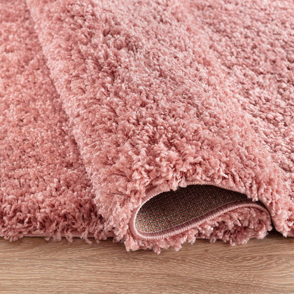 plain shaggy baby pink rug runner folded on wooden floor
