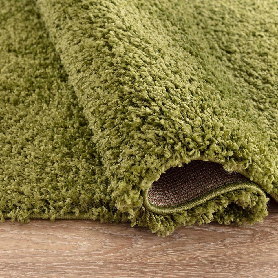 plain shaggy green circle rug folded on wooden floor