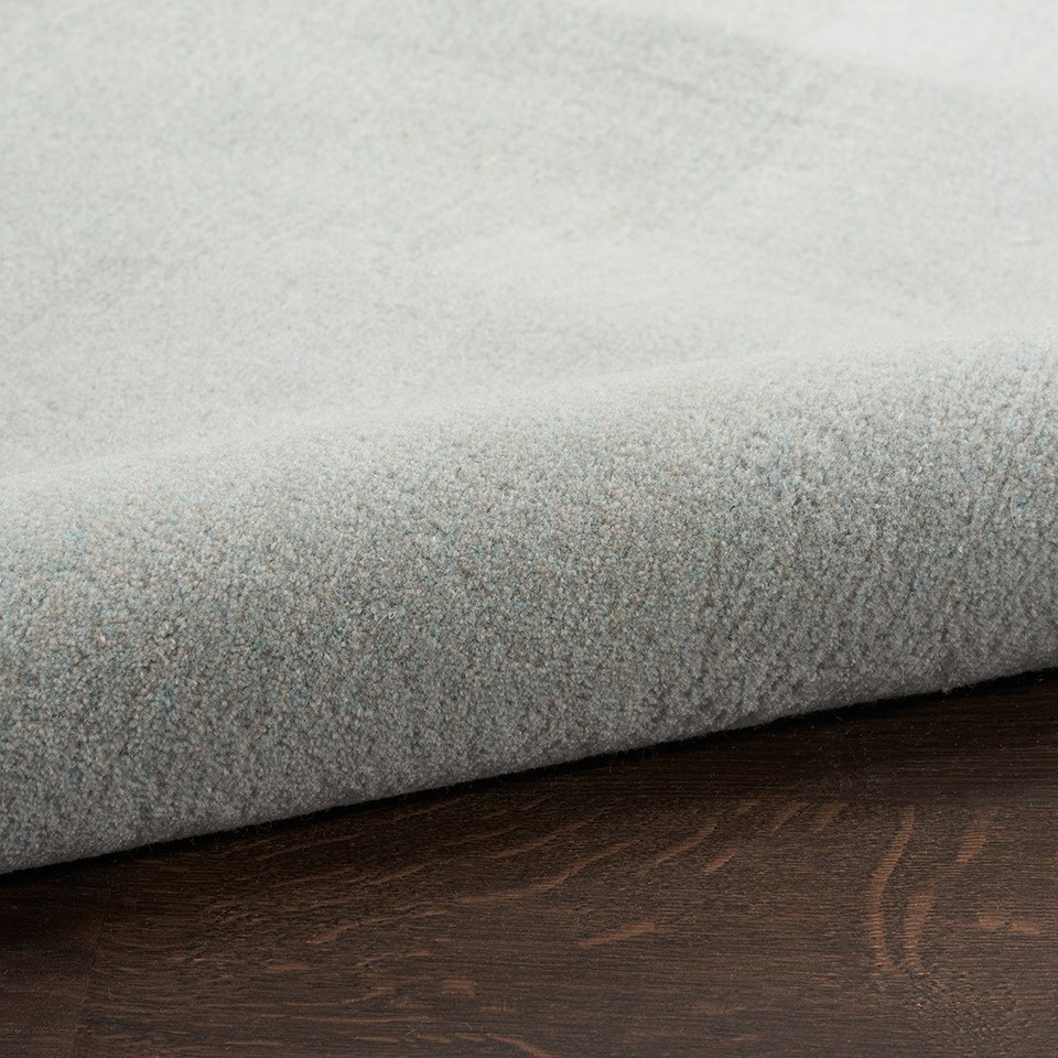 grey seafoam abstract rug partially rolled on a dark wood floor