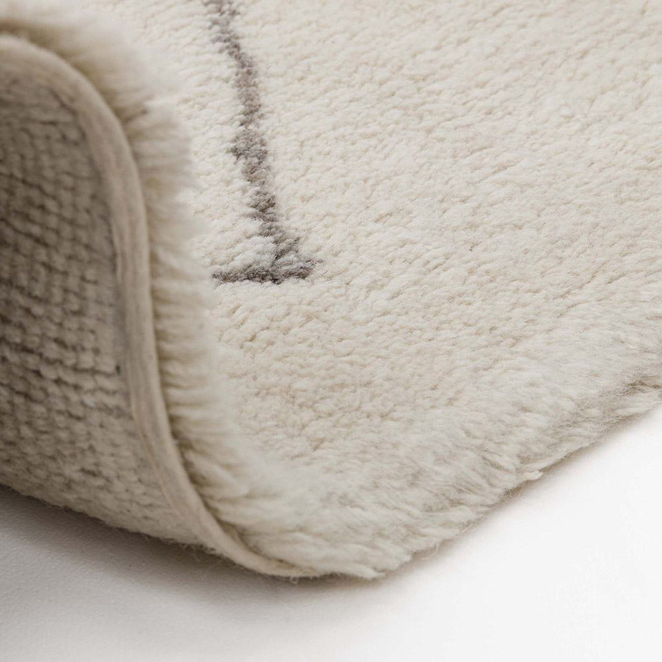 cream berber shaggy wool rug partially folded on white floor