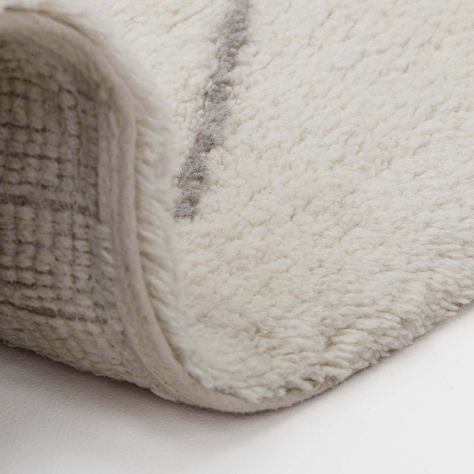 cream berber shaggy wool rug partially folded on white floor