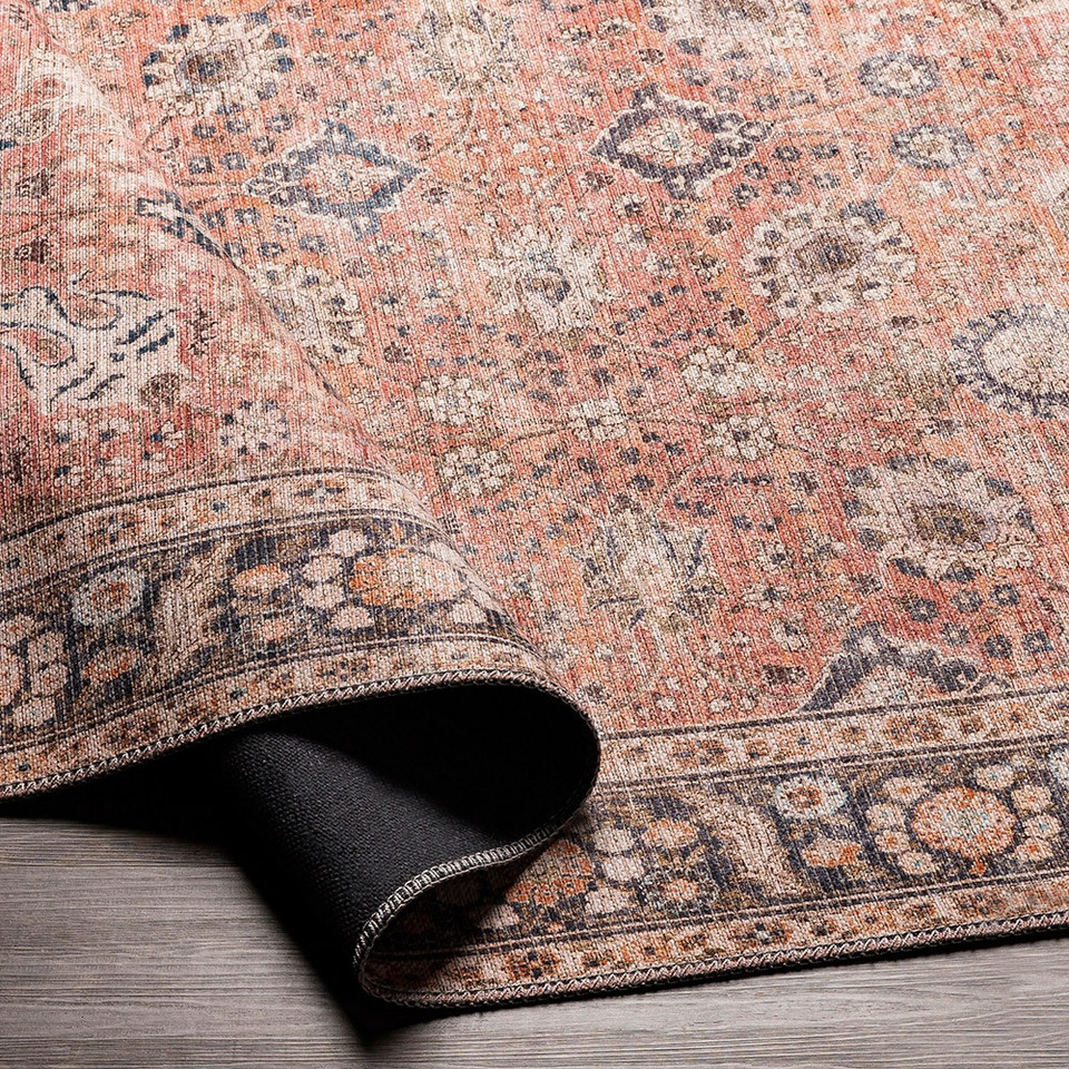 orange traditional rug partially folded on wood floor