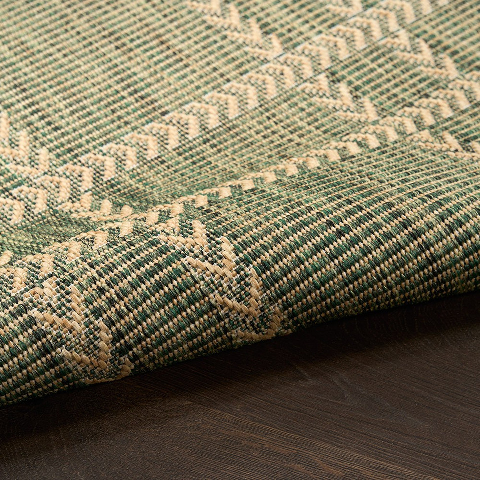 green geometric indoor outdoor rug partially rolled on wood floor