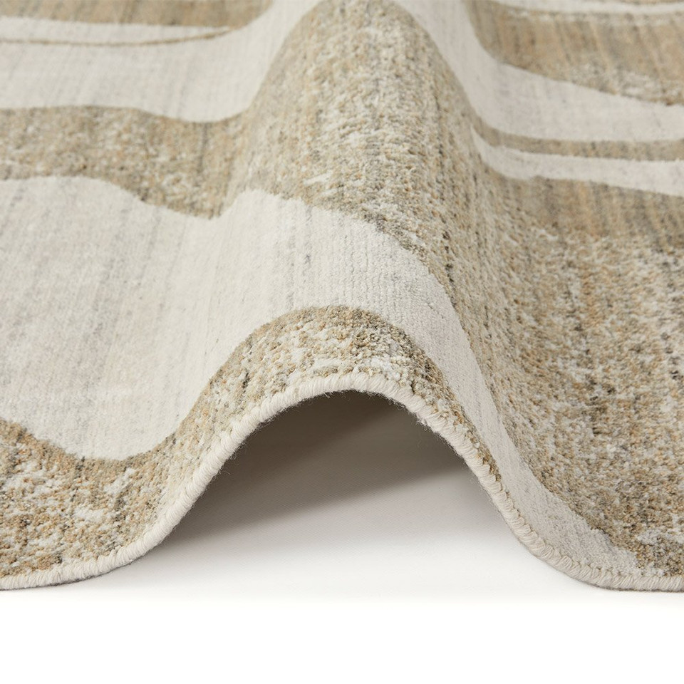 ivory mink abstract rug partially folded on a white floor