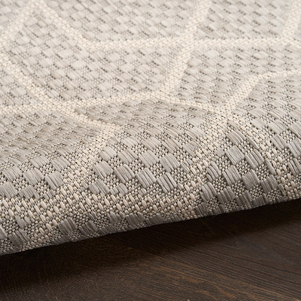 grey geometric indoor outdoor rug partially rolled on wood floor