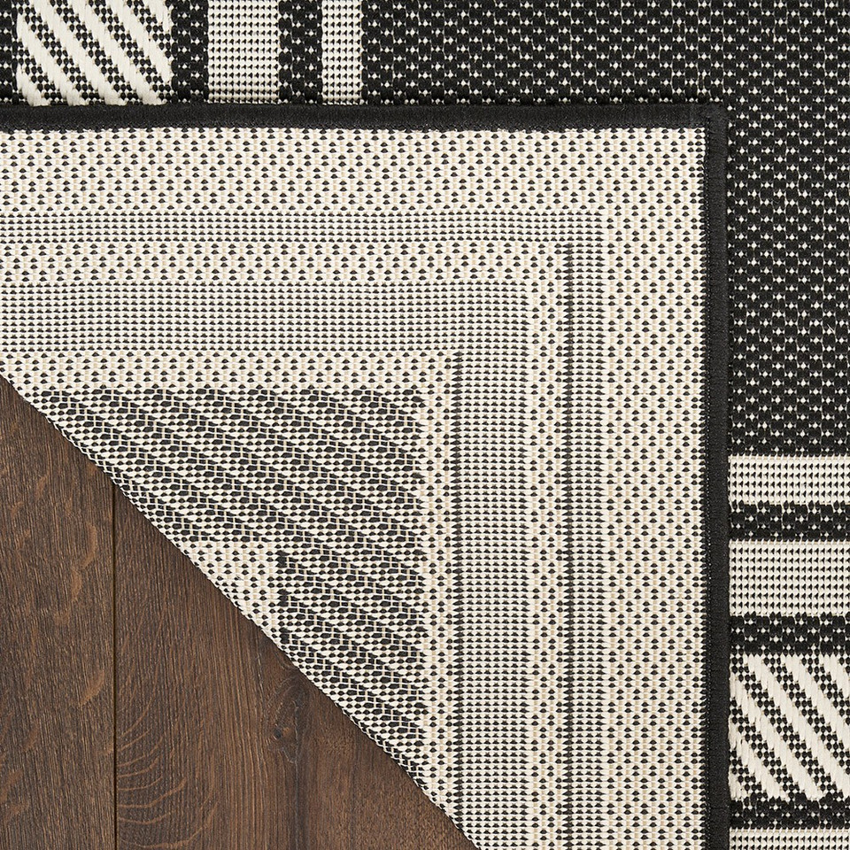 black geometric indoor outdoor rug folded on wood floor