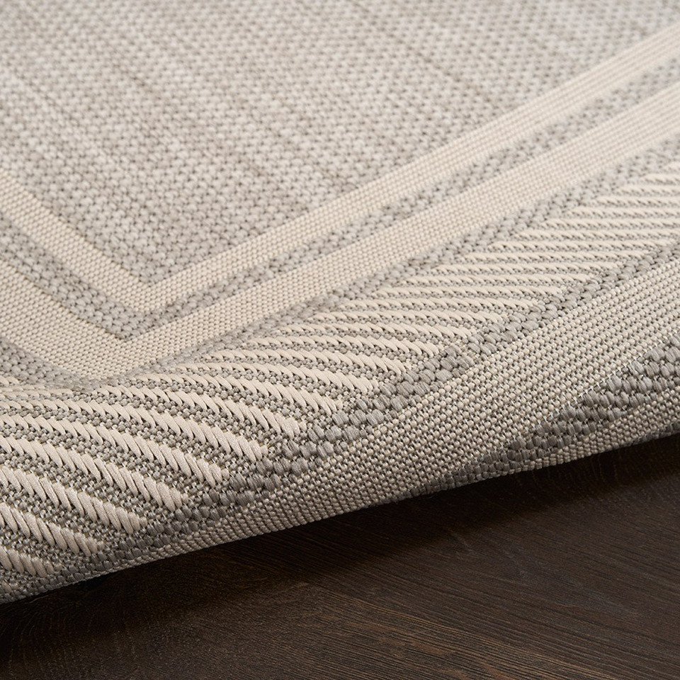 grey geometric indoor outdoor rug partially rolled on wood floor