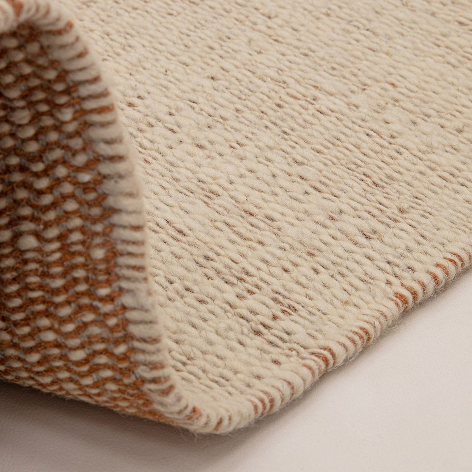 rust flatweave wool rug partial fold on white floor
