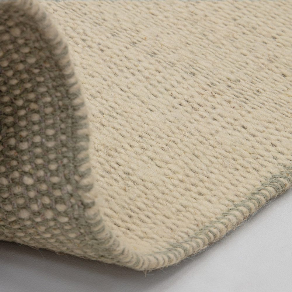 sage flatweave wool rug partial fold on white floor