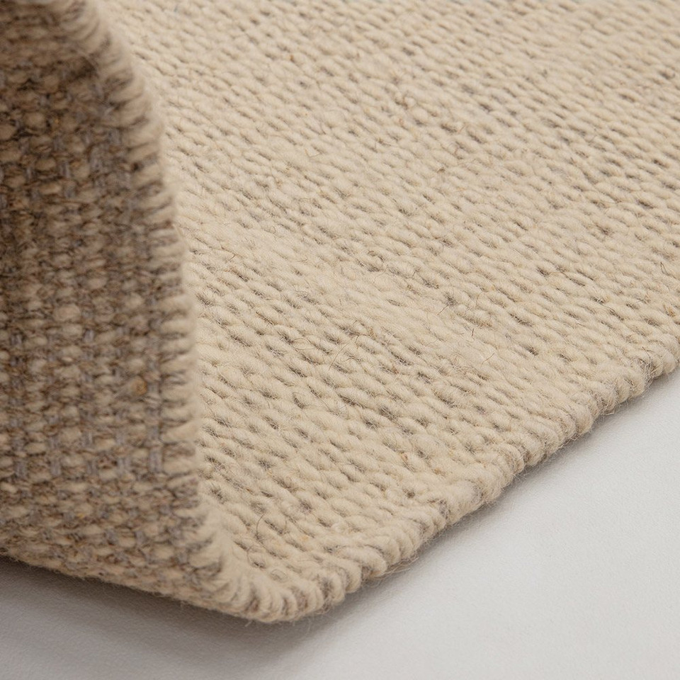 sand flatweave wool rug partial fold on white floor
