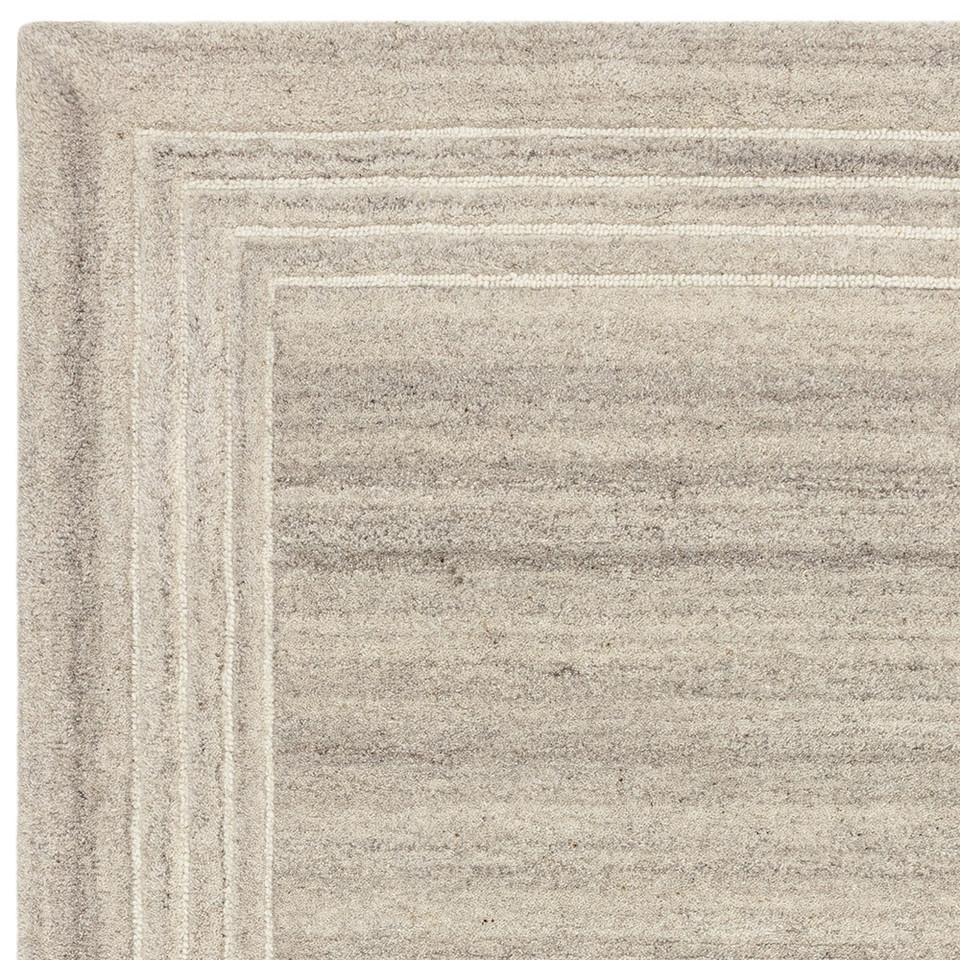 Overhead studio crop of a grey minimalist wool rug corner with structured off-white border accent framing the piece.