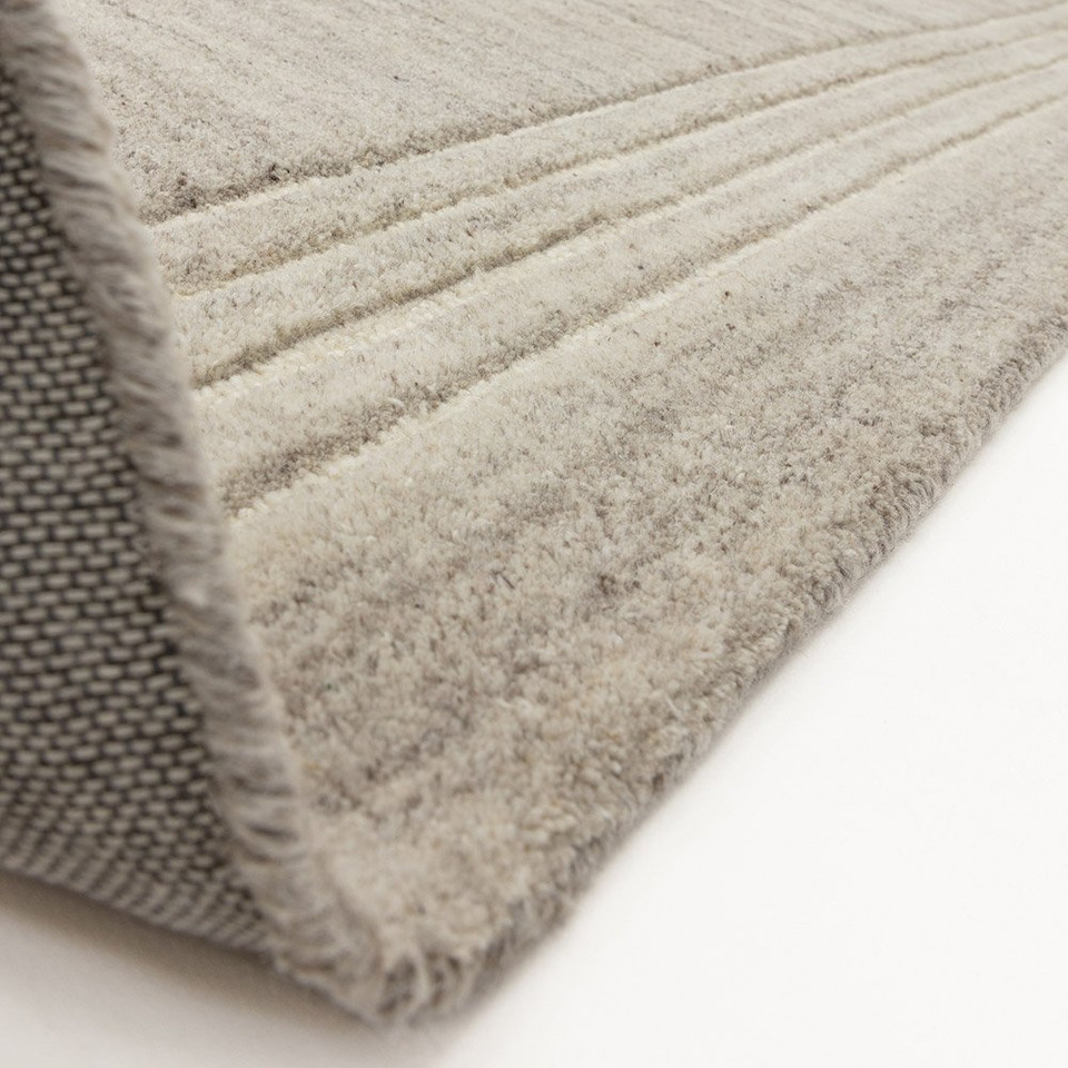 The underside and premium heavy canvas backing of a soft grey tufted wool area rug flipped at the corner.