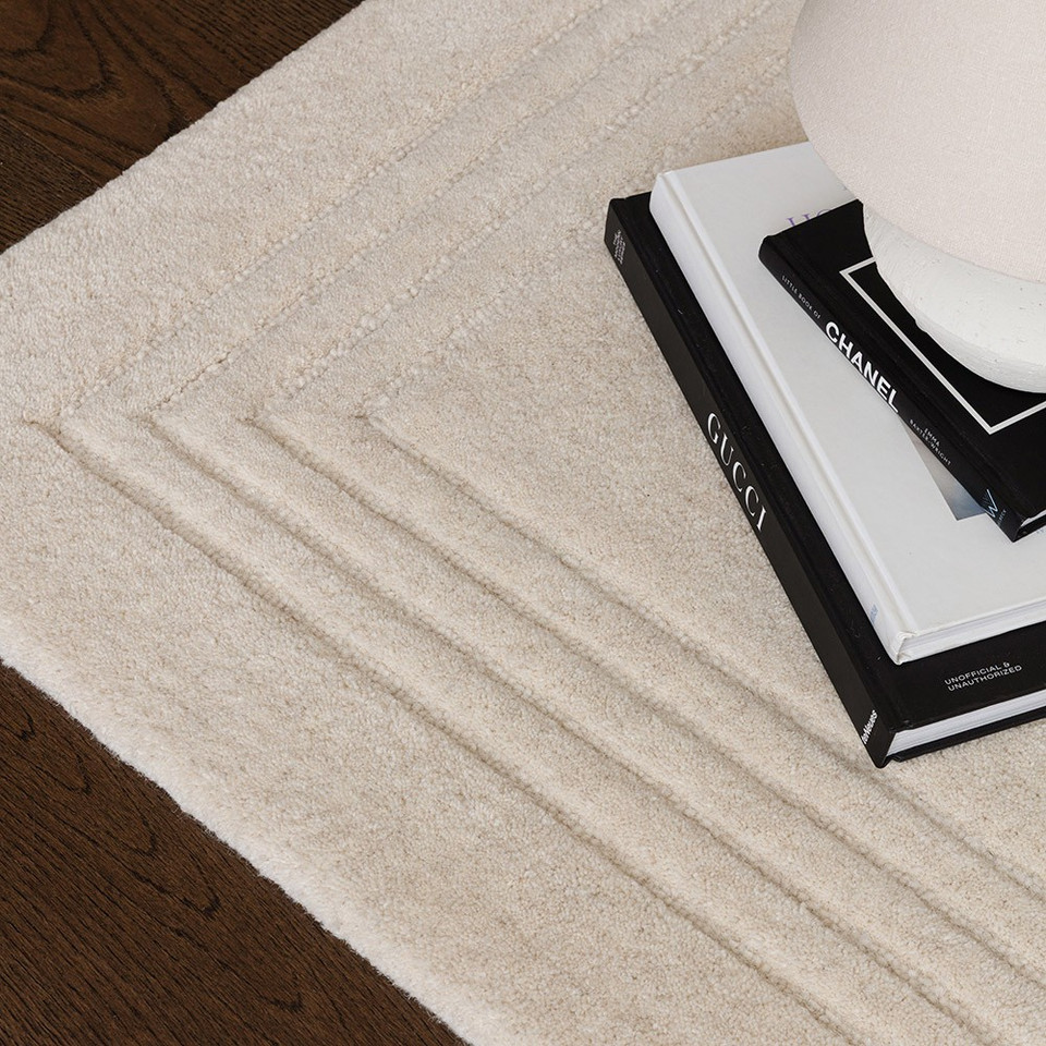Detailed corner view of a cream hand-tufted wool rug with thin dark border lines, styled next to a stack of hardcover books.