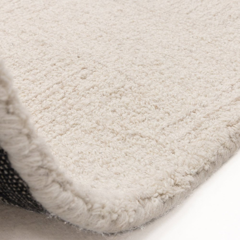 Flipped corner of the Theodore Hatch white and sand wool area rug, displaying its heavy canvas backing and soft, dense pile.