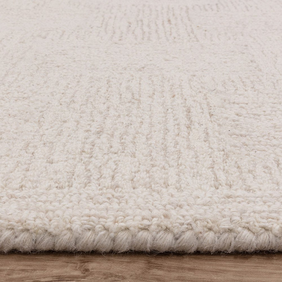 Close-up profile of the white and sand wool rug edge, highlighting the thick, woven pile texture and neat monochrome border.