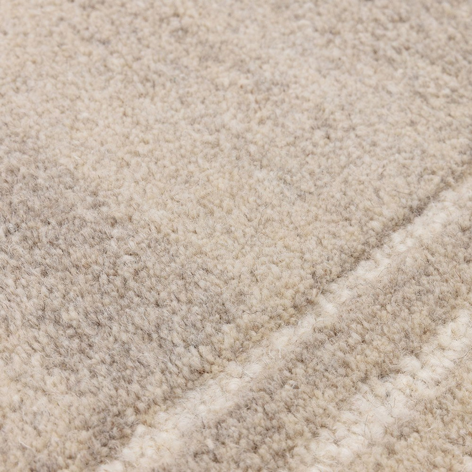Macro texture shot highlighting the tight, high-quality tufted weave and soft woolen fibers of a contemporary sand beige area rug.