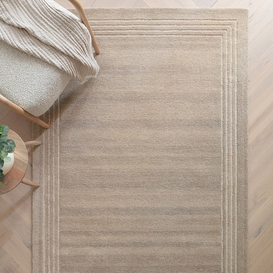 Earthy-toned living room interior featuring a luxury sand wool rug anchoring a minimalist layout with a modern wooden armchair.