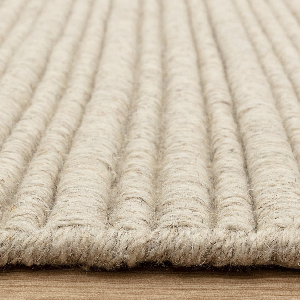 Side view detail of a textured cream wool rug highlighting its thick, durable linear construction.