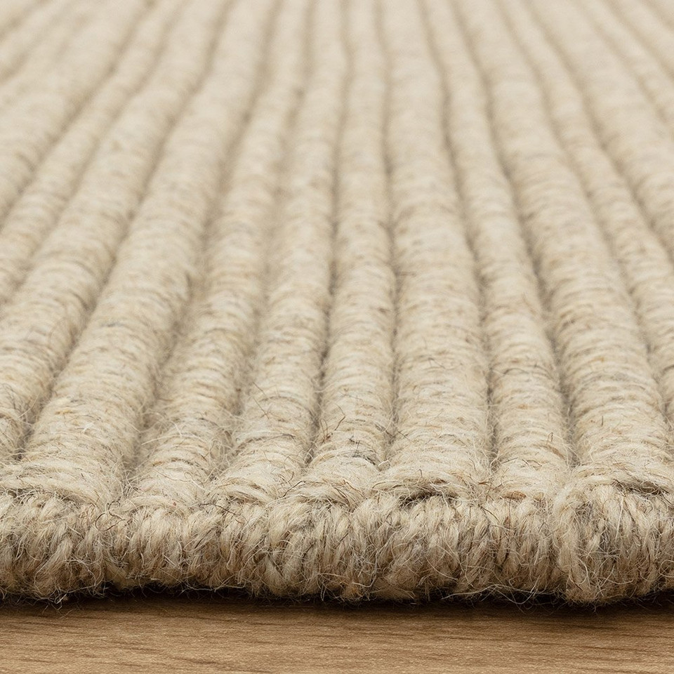 Side view detail of a textured neutral wool rug highlighting its thick, durable linear construction.