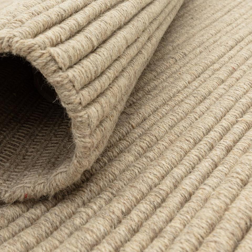 Close-up of a rolled beige wool rug demonstrating its flexibility, thickness, and natural yarn weave.