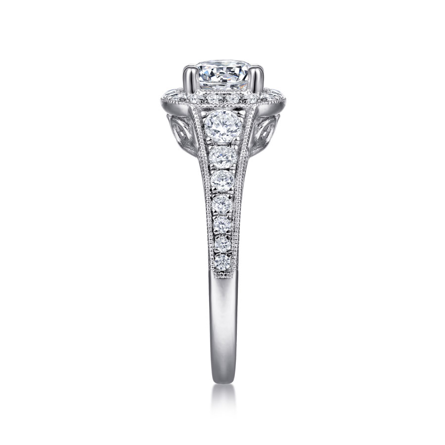 vintage-inspired halo engagement ring with round moissanite center stone and diamond accented halo and band with scrollwork detailing beneath the center stone