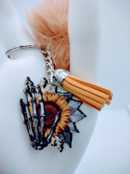 Introducing the sunflower hand acrylic keychain with fur and tassel. This unique keychain is a must-have accessory for any fashion-savvy individual. The sunflower hand features the image of a skeleton hand gently holding a sunflower. The acrylic keychain is crafted out of high-quality acrylic material that is durable and easy to clean. The keychain also comes with a matching fur and tassel accessory, which gives it a sophisticated look. Though the color of the fur may vary upon delivery due to availability, each keychain features an original unique design.