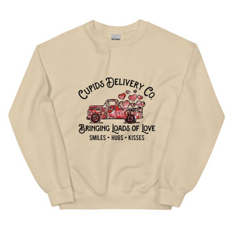 Crew neck sweatshirt in a neutral/pastel color featuring a pickup truck overflowing with red and pink hearts. Text reads “Cupid’s Delivery Co.: Bringing Loads of Love, Smiles, Hugs, and Kisses” in fun, playful lettering. Shown folded and on a flat lay with clear visibility of full design.