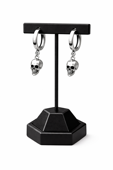 A pair of small silver skull huggie hoop earrings featuring polished metal hoops with detailed dangling skull charms. These lightweight earrings offer a subtle edgy look, combining minimalist size with gothic-inspired design. Perfect for everyday wear, they add a touch of alternative style while remaining versatile and easy to pair with any outfit.