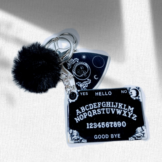 The centerpiece of this keychain is a miniaturized Ouija board, reminiscent of the ancient divination tool that has intrigued and fascinated for centuries. Its intricate design captures the essence of mystery and invites you to explore the unknown. Adding a dash of charm, this keychain features a soft and fluffy pom-pom, playfully dangling alongside the Ouija board. And that's not all! For those who appreciate the darker aesthetics, we've included a captivating black moon charm. Its intricate details and mesmerizing presence are sure to spark conversations and intrigue among your friends and acquaintances.