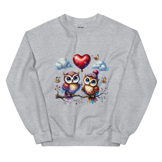 Crew neck sweatshirt shown flat featuring two pastel-colored owls sitting on a branch with a heart-shaped balloon between them. Design uses soft Valentine pastel tones with a cute, cozy aesthetic.