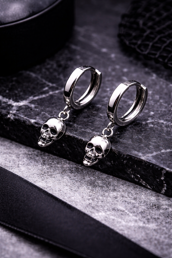 A pair of small silver skull huggie hoop earrings featuring polished metal hoops with detailed dangling skull charms. These lightweight earrings offer a subtle edgy look, combining minimalist size with gothic-inspired design. Perfect for everyday wear, they add a touch of alternative style while remaining versatile and easy to pair with any outfit.