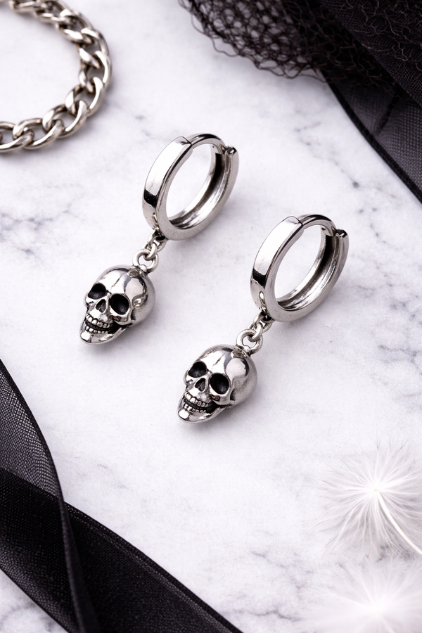 A pair of small silver skull huggie hoop earrings featuring polished metal hoops with detailed dangling skull charms. These lightweight earrings offer a subtle edgy look, combining minimalist size with gothic-inspired design. Perfect for everyday wear, they add a touch of alternative style while remaining versatile and easy to pair with any outfit.