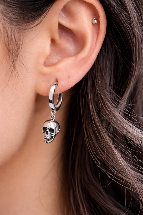 A pair of small silver skull huggie hoop earrings featuring polished metal hoops with detailed dangling skull charms. These lightweight earrings offer a subtle edgy look, combining minimalist size with gothic-inspired design. Perfect for everyday wear, they add a touch of alternative style while remaining versatile and easy to pair with any outfit.