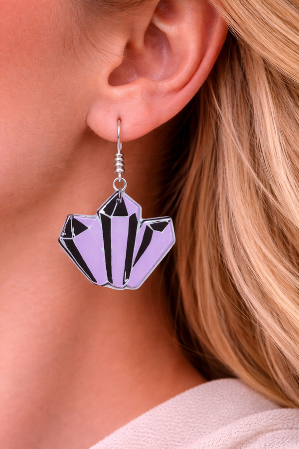 A curated collection of witchy-inspired acrylic earrings featuring dark, mystical designs including celestial symbols, occult figures, crystal shapes, and gothic motifs. Each pair showcases bold black detailing paired with soft lavender accents, displayed in styled scenes with crystals, candles, and moody textures. The collection blends alternative fashion with mystical aesthetics, creating a cohesive, edgy yet feminine visual