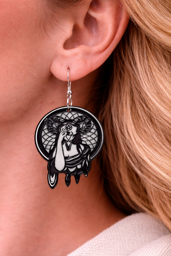 A curated collection of witchy-inspired acrylic earrings featuring dark, mystical designs including celestial symbols, occult figures, crystal shapes, and gothic motifs. Each pair showcases bold black detailing paired with soft lavender accents, displayed in styled scenes with crystals, candles, and moody textures. The collection blends alternative fashion with mystical aesthetics, creating a cohesive, edgy yet feminine visual