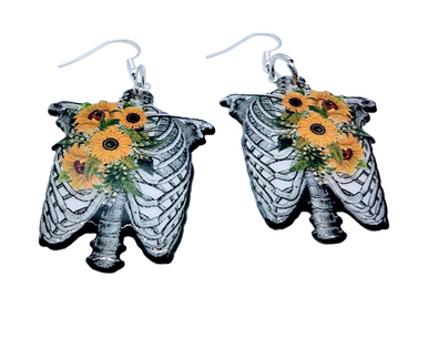 Assorted sunflower-themed acrylic earrings featuring bright yellow petals with dark centers and earthy accents. Each design highlights a rustic, nature-inspired look with bold outlines and clean detailing, displayed on silver fishhook ear wires against a neutral background.