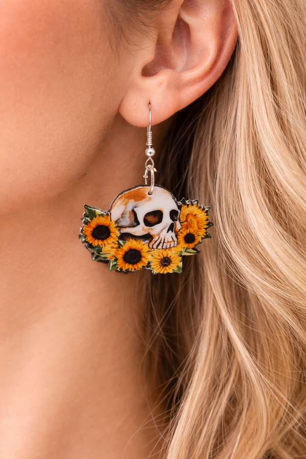 Assorted sunflower-themed acrylic earrings featuring bright yellow petals with dark centers and earthy accents. Each design highlights a rustic, nature-inspired look with bold outlines and clean detailing, displayed on silver fishhook ear wires against a neutral background.