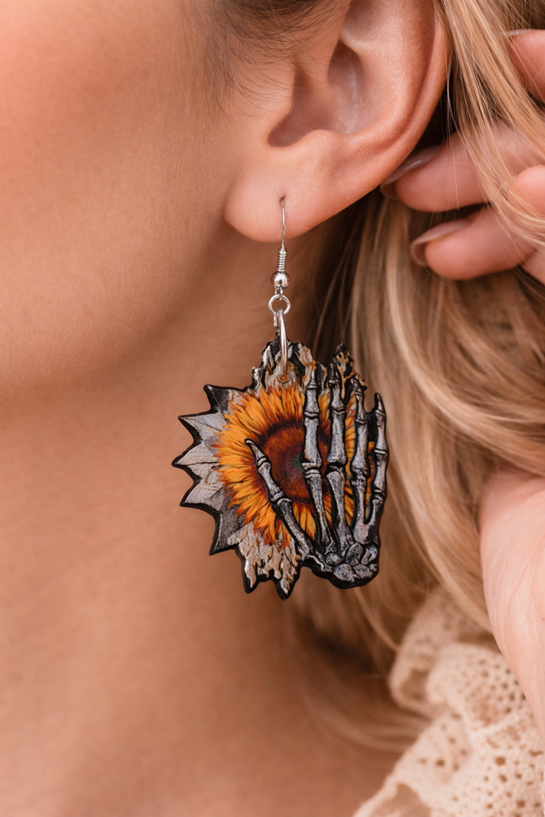 Assorted sunflower-themed acrylic earrings featuring bright yellow petals with dark centers and earthy accents. Each design highlights a rustic, nature-inspired look with bold outlines and clean detailing, displayed on silver fishhook ear wires against a neutral background.