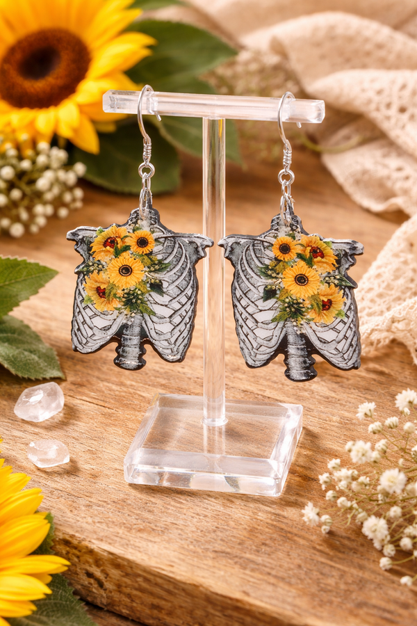 Assorted sunflower-themed acrylic earrings featuring bright yellow petals with dark centers and earthy accents. Each design highlights a rustic, nature-inspired look with bold outlines and clean detailing, displayed on silver fishhook ear wires against a neutral background.