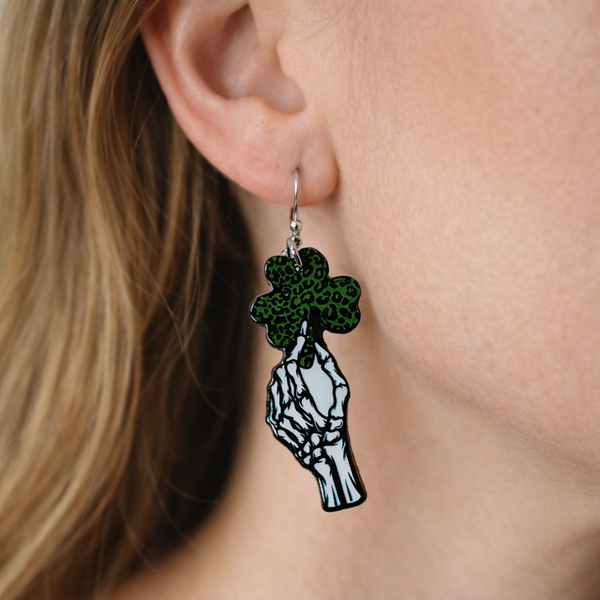 An assorted collection of St. Patrick’s Day-themed acrylic earrings featuring bold, edgy designs with skeletons, skulls, shamrocks, and leprechaun-inspired elements. Each pair showcases vibrant green accents paired with black and white detailing for a high-contrast, gothic-meets-festive aesthetic. Designs include skeleton hands, skull faces, clover details, and playful drinking motifs, all hanging from silver fishhook ear wires. This set blends dark humor, alternative style, and holiday spirit for a unique, statement-making accessory lineup.