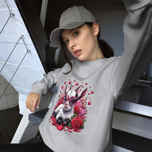 Crew neck sweatshirt shown flat featuring a cute goat wearing heart-shaped sunglasses, surrounded by Valentine hearts and floral accents. Design uses soft pastel tones and has no wording.