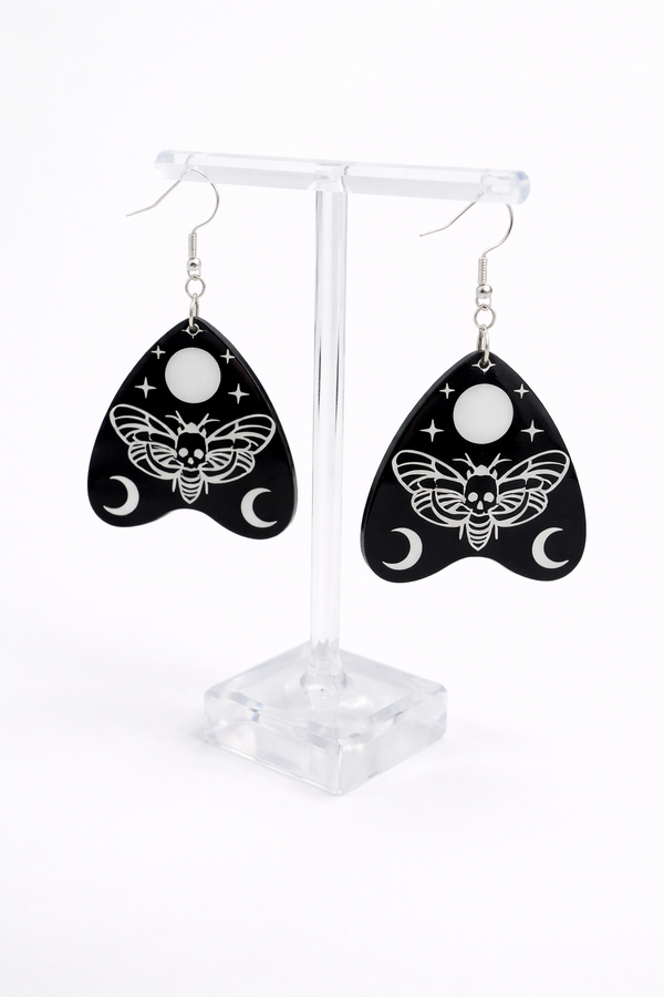 Collection of Ouija planchette acrylic earrings displayed in multiple design variations on a clean background. Each pair features unique lettering styles, symbols, and finishes while maintaining a cohesive dark, witchy aesthetic. The assortment highlights different options within the same occult-inspired theme.