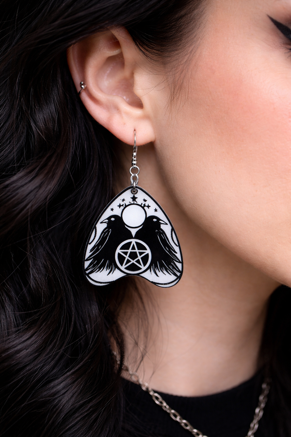 Collection of Ouija planchette acrylic earrings displayed in multiple design variations on a clean background. Each pair features unique lettering styles, symbols, and finishes while maintaining a cohesive dark, witchy aesthetic. The assortment highlights different options within the same occult-inspired theme.