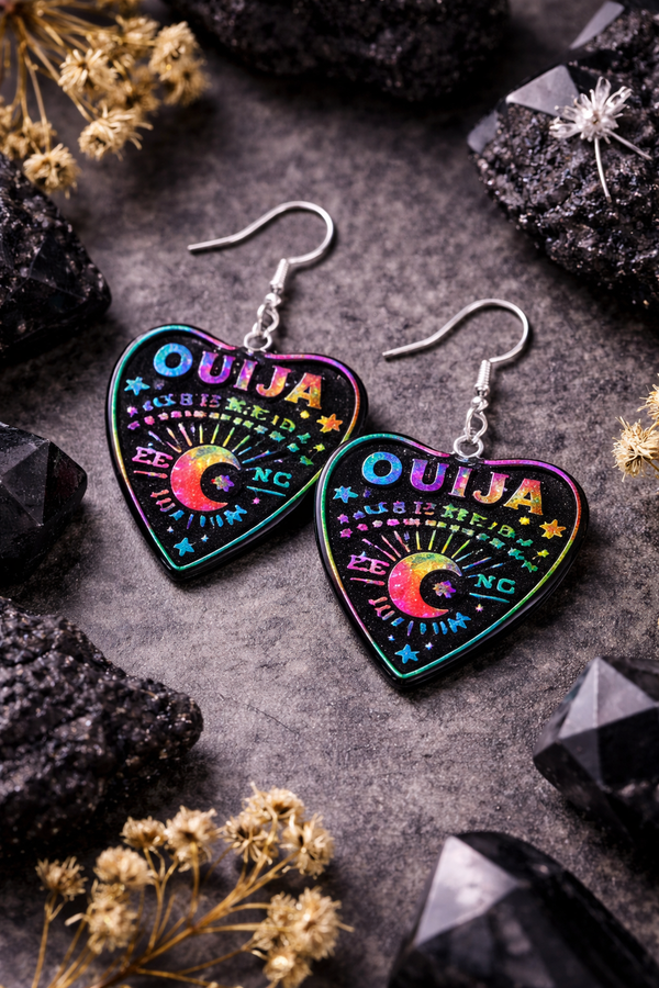 Collection of Ouija planchette acrylic earrings displayed in multiple design variations on a clean background. Each pair features unique lettering styles, symbols, and finishes while maintaining a cohesive dark, witchy aesthetic. The assortment highlights different options within the same occult-inspired theme.