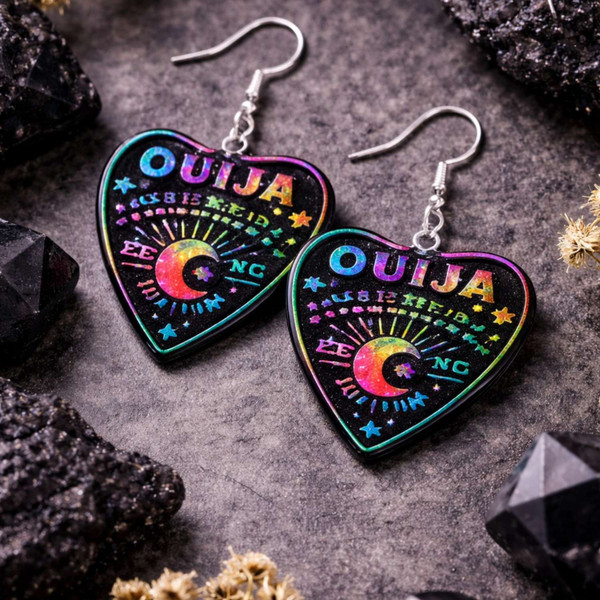 Collection of Ouija planchette acrylic earrings displayed in multiple design variations on a clean background. Each pair features unique lettering styles, symbols, and finishes while maintaining a cohesive dark, witchy aesthetic. The assortment highlights different options within the same occult-inspired theme.