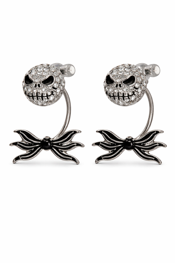 Features skull stud earrings with a separate spider bow backing designed to sit behind the ear, creating a layered, dimensional look. Images include clean white background product shots for detail, a stand display for structure, an on-ear lifestyle photo to show fit and placement, and a dark, moody flat lay to highlight the gothic aesthetic and sparkle.