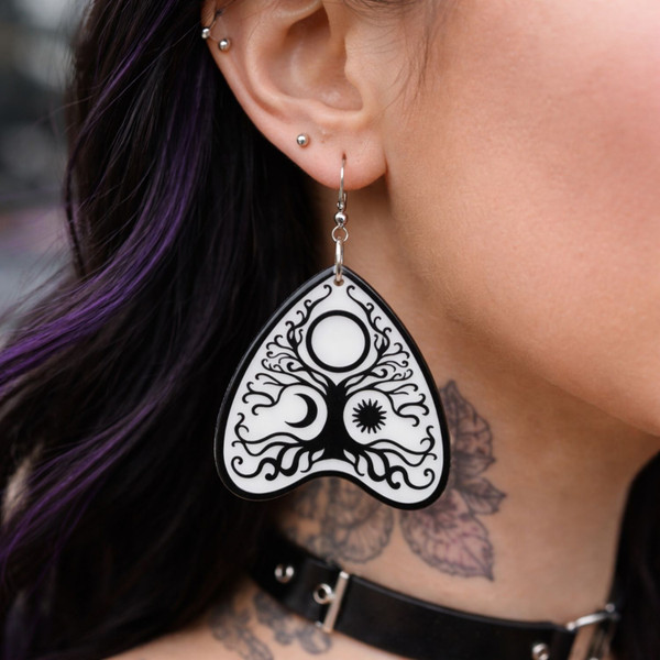 Collection of Ouija planchette acrylic earrings displayed in multiple design variations on a clean background. Each pair features unique lettering styles, symbols, and finishes while maintaining a cohesive dark, witchy aesthetic. The assortment highlights different options within the same occult-inspired theme.