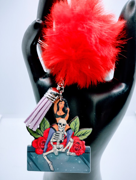 Love Acrylic Keychain With Fur And Tassel. Rose covered image of a sexy lady. Acrylic Keychain is made with 100% premium acrylic and features a sexy lady on the shoulders of her skeleton lover. This keychain makes the perfect gift for all spooky scene lovers. Our designers carefully choose every material to bring you the best quality and craftsmanship possible. Though the color of the fur may vary upon delivery due to availability, each keychain features an original unique design.