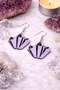 A curated collection of witchy-inspired acrylic earrings featuring dark, mystical designs including celestial symbols, occult figures, crystal shapes, and gothic motifs. Each pair showcases bold black detailing paired with soft lavender accents, displayed in styled scenes with crystals, candles, and moody textures. The collection blends alternative fashion with mystical aesthetics, creating a cohesive, edgy yet feminine visual